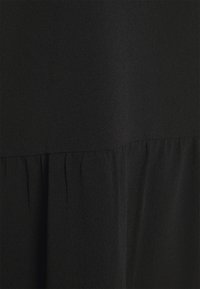 Tissu noir avec une surface subtilement texturée et un détail de couture froncée créant des plis doux.