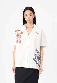 Chemise à col à manches courtes en tissu blanc cassé ornée de motifs abstraits orange et marine. L'avant présente un détail logo en or.
