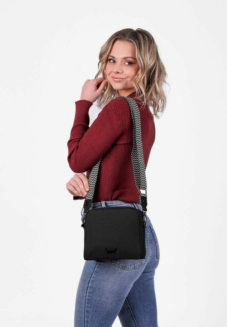 Černá crossbody taška s texturovaným povrchem, vybavená vzorovaným, nastavitelným popruhem a malým logem na přední části.