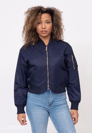 Giacca bomber blu navy con zip dorata, polsini e orlo a coste. Presenta dettagli ricamati sul petto e una tasca laterale sulla manica.