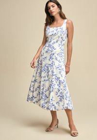 Blommig midi-klänning med fyrkantig halsringning, vitt tyg med blå blommönster, utsvängd kjol och en slät yta. Matchad med nude-hängslen.
