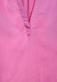 Primo piano di un tessuto rosa con scollatura a V e cuciture dettagliate attorno all'area del colletto.