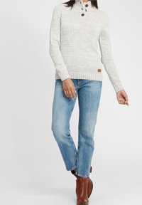 Lichtgrijze gebreide trui met een hoge kraag, drie bruine knopen en geribbelde manchetten, gecombineerd met lichtblauwe rechte jeans en bruine enkellaarsjes.