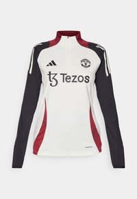 Fehér, hosszú ujjú trikó magas gallérral, fekete és piros kiegészítőkkel, a Manchester United logójával és a Tezos márkajelzésével. Aeroready anyag.