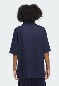 Camicia a maniche corte blu navy con un design testurizzato e perforato. Presenta un colletto classico e una vestibilità ampia, che si estende fino a metà fianchi.
