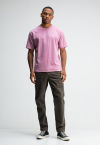 Korte mouwen, lichtroze katoenen T-shirt met een klein logo, gecombineerd met donkergroene broeken en zwart-witte canvas sneakers.