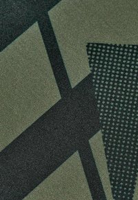Acercamiento a una tela con formas geométricas abstractas en verde oscuro y negro, con un patrón texturizado y líneas que se cruzan.