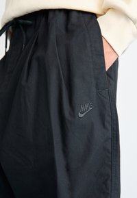 Μαύρο παντελόνι Nike με ελαστική μέση και κορδόνι, που διαθέτει ένα διακριτικό κεντημένο λογότυπο στο μπροστινό μέρος. Απαλή, ελαφριά ύφανση.