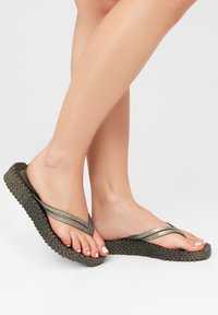 Donkergroene flip-flops met metallic zilveren banden, met een geweven textuur en een gevormde voetbed, die een minimalistisch ontwerp uitstralen.