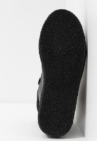 Black athletic shoe sole with a textured rubber finish, featuring a curved shape and minimalistic design, positioned against a white background.