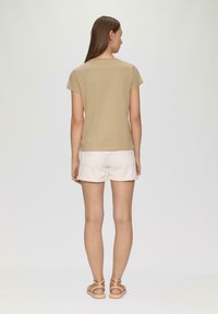 Tan gekleed T-shirt met korte mouwen, gecombineerd met witte denim shorts. Model draagt lichtbeige sandalen. Zachte textuur, minimalistisch ontwerp.
