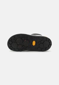 Suela de goma negra con un patrón hexagonal y motas naranjas. Presenta un logo de Vibram amarillo y elementos de tracción pronunciados.
