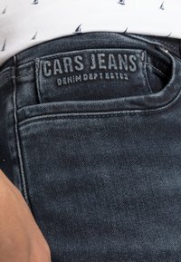 Donkerblauwe spijkerbroek met een zichtbare achterzak, voorzien van een leren label met de tekst "CARS JEANS" en gestructureerde stiksels.