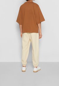 Camiseta marrón de gran tamaño con mangas cortas, combinada con pantalones tapered color crema y zapatillas blancas. Diseño simple, corte relajado.