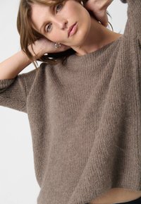 Brun strikket sweater med ribbet tekstur, bred bådudskæring og afslappet pasform. Blødt materiale, cropped længde og ærmer til albuen.