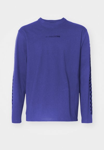 T-shirt à manches longues en coton violet, avec un col rond et un motif le long des manches, accompagné d'un logo sur la poitrine.
