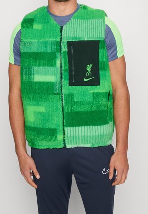 Mann trägt eine grüne, gemusterte Fleeceweste mit einer schwarzen Reißverschlusstasche mit den Logos von Liverpool FC und Nike, über einem kurzärmligen Sportshirt.