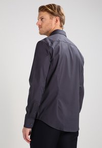 Dark gray button-up shirt with a smooth texture, slim fit, pointed collar, and long sleeves. Features subtle stitching and cuff buttons.
