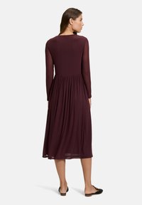 Maronfarbendes A-Linien-Kleid, lange durchsichtige Ärmel, geraffte Taille, fließender Stoff, knielang mit glatter Textur und Rückansicht.