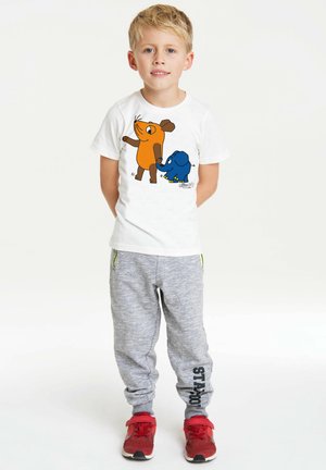 White t-shirt with colorful cartoon design of an orange animal and a blue elephant. Grey sweatpants with black lettering. Red sneakers.
