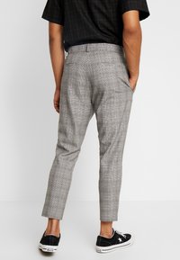 Pantalons à carreaux gris coupe slim, avec une texture lisse, deux poches arrière, portés avec des baskets en toile noires.