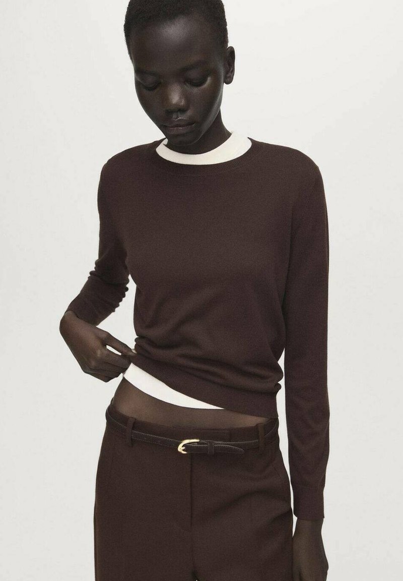 Brown knit sweater with white crew neckline, long sleeves, paired with dark trousers and a black belt featuring a gold buckle detail.