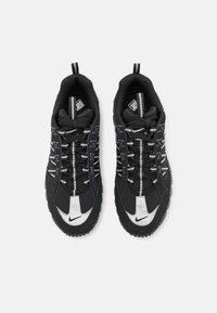 Black athletic shoes with textured fabric upper, white accents on the toe and branding, and reflective laces for visibility. Rubber outsole features traction.