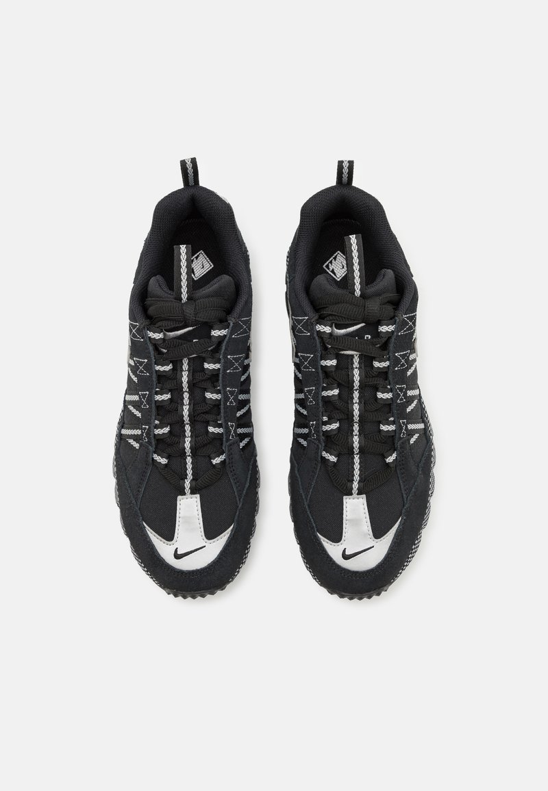 Baskets de sport noires avec une tige en tissu texturé, des accents blancs sur le bout et le logo, et des lacets réfléchissants pour la visibilité. La semelle extérieure en caoutchouc offre une bonne traction.