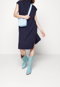 Abito in maglia blu marina con colletto alto e spacco laterale, abbinato a stivali da cowboy azzurri chiari con dettagli di ricamo e una borsa a tracolla coordinata.