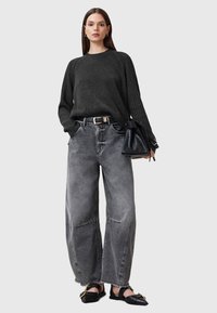 Sweter z prążkowanej dzianiny w kolorze węglowym, szare dżinsy o szerokiej nogawce z postrzępionym końcem, czarne buty typu slip-on oraz mała czarna torebka na ramię.