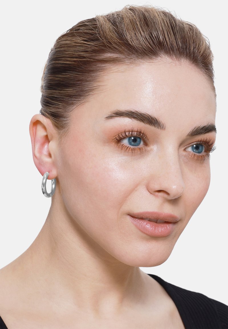 Orecchino a cerchio in argento con finitura lucida, forma circolare, dimensione media, indossato all'orecchio di un modello, evidenziando la sua texture liscia e la superficie riflettente.