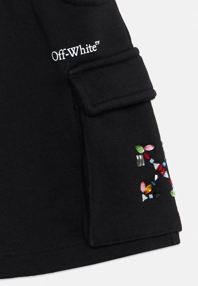 Μαύρο ύφασμα με λευκό κείμενο "Off-White™" κοντά σε μια τσέπη διακοσμημένη με πολύχρωμες διακοσμήσεις που μοιάζουν με πολύτιμους λίθους στο μανίκι.