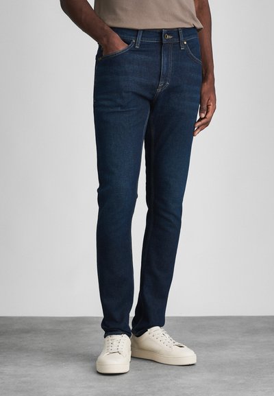 Donkerblauwe jeans van denim, met een slim fit, vijf-pocket ontwerp, subtiele stiksel en gecombineerd met witte sneakers.
