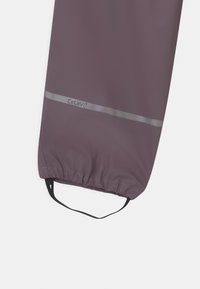 Waterdichte paarse jas met een verzamelde manchet, reflecterende grijze streep en zwarte lus om op te hangen. Bevat het merkje "Celavi."