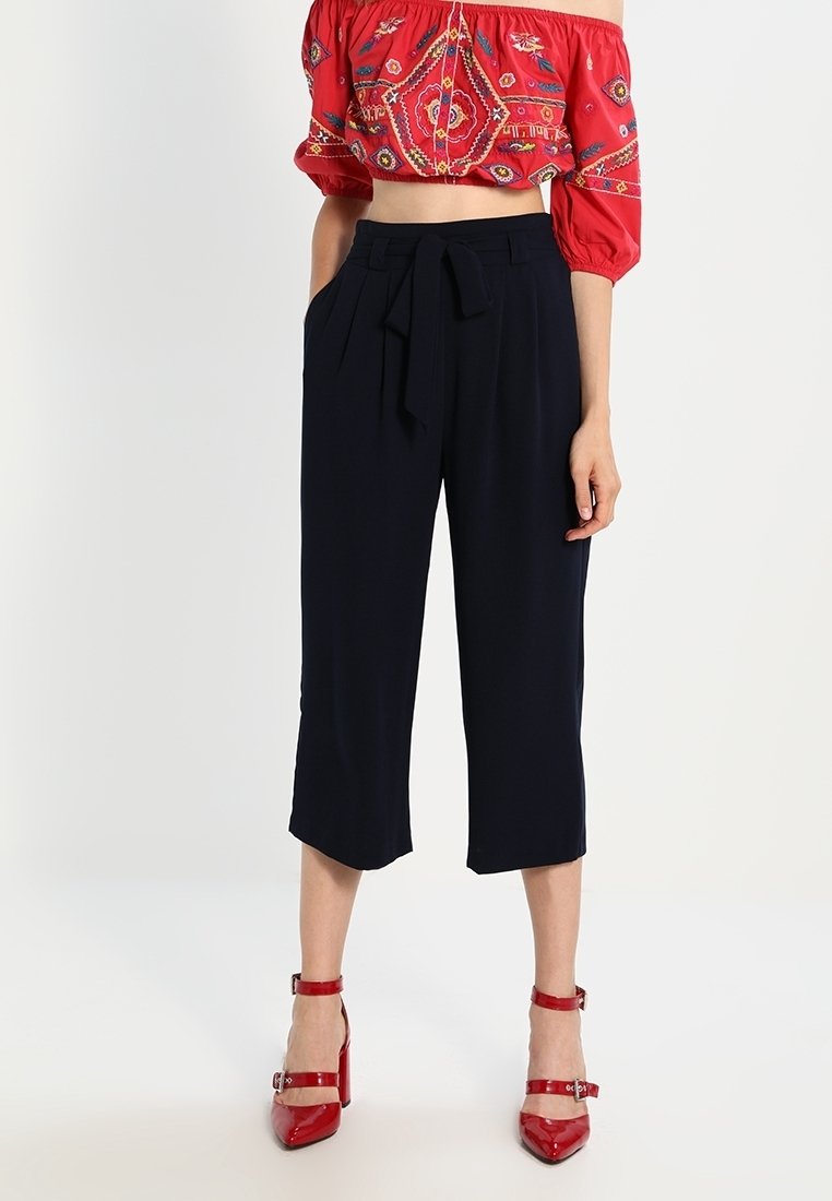 Marinblå cropped byxor med knytmidja, med två sidofickor och en mjuk textur. Matchas med en röd broderad crop top och röda klackar.