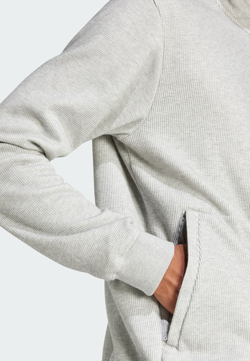 Szary, teksturowany sweatshirt z żebrowanym wzorem, długimi rękawami i kieszenią z przodu. Posiada subtelne przeszycia i elastyczne mankiety.