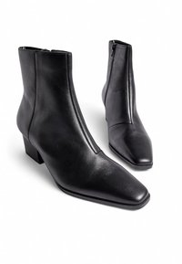 Musta nahkasaapas nilkkamallia, teräväkärkinen ja matala lohkoilu. Sivussa vetoketju kiinnitystä varten ja sileä, matta pinta.