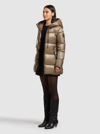 Vatteret jakke i metallisk beige med hætte, lynlåslukning foran, sidelommer og elastiske snore. Sat sammen med en sort kjole og støvler til knæet.