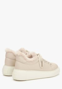 Beige Leder-Sneaker mit einem flauschigen, weichen Kragen und weißer Gummisohle. Merkmale sind die abgerundete Form, Schnürsenkel und silberfarbene Ösen.
