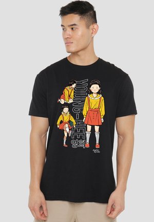 A man in a black t-shirt featuring colorful cartoon illustrations of a girl in a yellow outfit, paired with bold text reading "YOUNG-HEE."