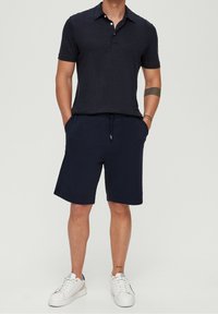 Polo bleu marine avec une finition texturée, associé à un short bleu marine avec poches latérales et cordon de serrage, complété par des baskets blanches.