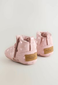 Stivaletti in suede rosa con dettagli a forma di cuore, fodera morbida e una patch in tessuto con logo sul tallone. Presentano un cinturino per un facile indossamento.