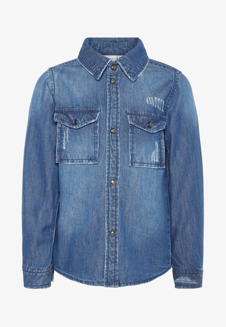 Chemise en denim bleu à manches longues avec fermeture boutonnée à l'avant, deux poches poitrine boutonnées, et détails d'usure légère subtile sur les poches et près du col.