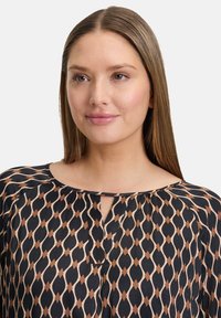 Czarna i beżowa bluzka w wzory z dekoltem w kształcie łezki, wykonaną z miękkiego materiału i o zwiewnym kroju z diamentowymi kształtami na całej powierzchni.