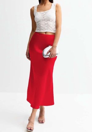 Femme portant un crop top blanc texturé sans manches, une jupe midi rouge, une pochette argentée métallique et des sandales à talons hauts à brides.