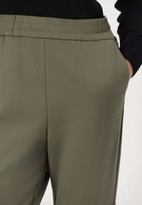 Pantalones deportivos de color verde oliva con cintura elástica y bolsillos laterales, fabricados en una tela ligera y suave. Diseño simple con líneas limpias.