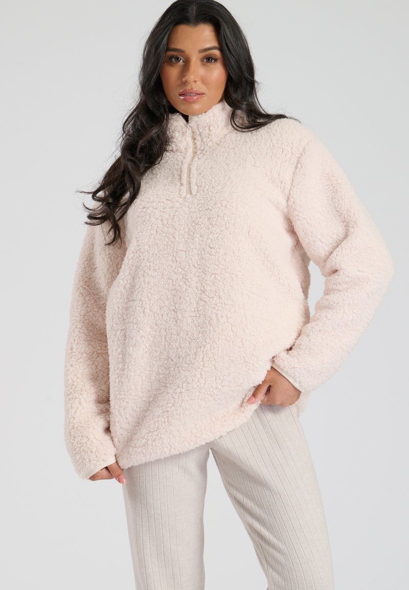 Lyserød fleecepullover med høj hals, halv lynlås og oversized pasform. Den har en blød, struktureret overflade og lange ærmer.
