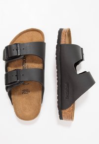 Svarta lädersandaler med två justerbara spännen, korkfotbädd och strukturerad gummisula. Varumärket "Birkenstock" präglat.