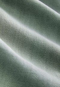 Közelkép világoszöld szövött anyagról, amely átlós serclimintával rendelkezik, és enyhe redők lágy árnyékokat hoznak létre.