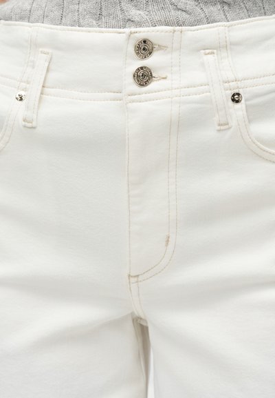 Λευκό παντελόνι από τζιν με διπλό κλείσιμο με ασημένια κουμπιά, θηλιές για ζώνη, μπροστινές τσέπες και μπεζ ραφές, φορεμένο με γκρι πλεκτό τοπ.